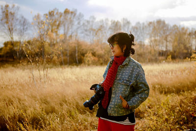 Woman holding camera looking away while standing on land