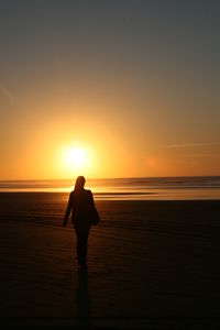 Silhouette man standing on beach against sky during sunset