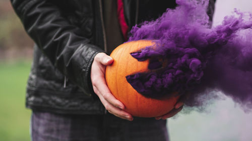 Midsection of man holding pumpkin while standing by purple flower