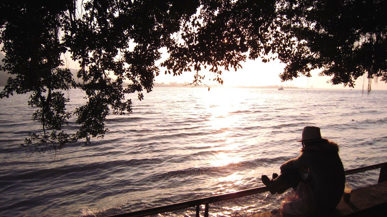 SILHOUETTE MAN SITTING BY TREE AGAINST SEA