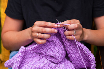 Close-up young woman in black t-shirt knits with knitting needles lilic sweater 