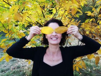 Full length portrait of a smiling young woman holding autumn leaves