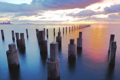 Wooden posts in sea against sky at sunset