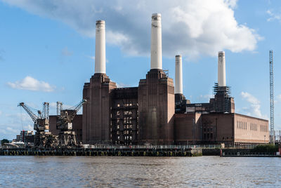 Factory by river against sky