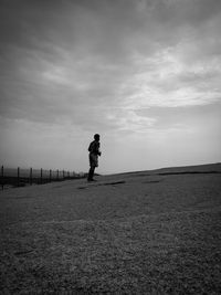 Side view of man standing on field against sky