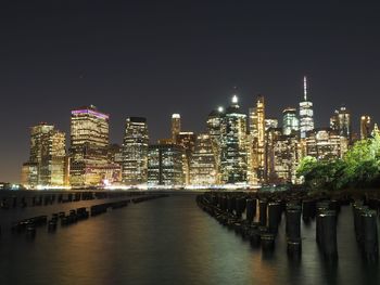 Illuminated buildings by river against sky at night