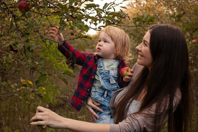 Beautiful mom and her son walking and picking apples in the garden. harvesting. autumn. apple orchar