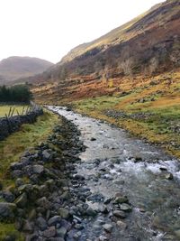 Stream flowing through land against sky