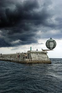 People at pier in sea against cloudy sky