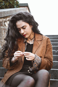 Young woman looking away while sitting on smart phone