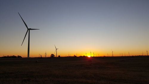Windmills on field against clear sky during sunset