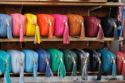 Many identical bags made of genuine leather but different colors displayed on the shelves of a store