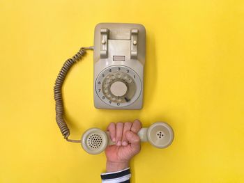 Midsection of person holding camera against yellow wall