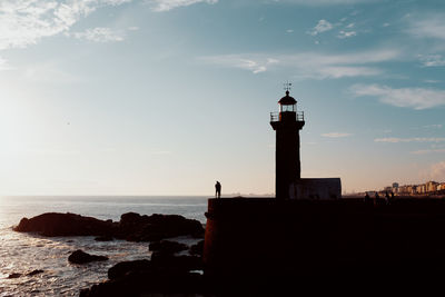 Silhouette lighthouse by sea against sky