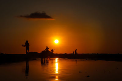Silhouette people riding on sea against sky during sunset