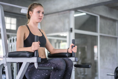 Athlete sporty woman exercising arm on machine builder muscles in fitness gym.