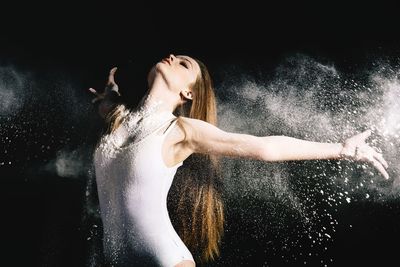 Portrait of young woman standing against black background