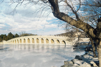 Arch bridge over river against sky during winter