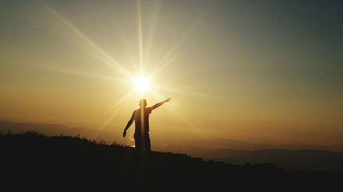 Silhouette man with arms outstretched standing against sky during sunset