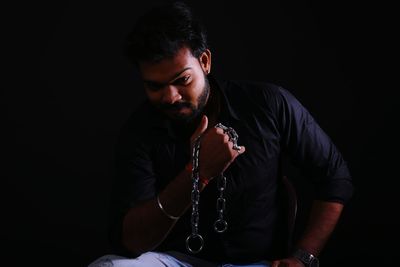 Young man sitting against black background