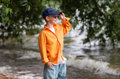 A boy in an orange shirt on the seashore. a child in sunglasses person