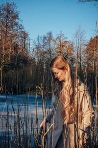 Woman looking at lake by trees against clear sky