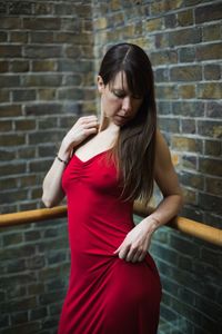 Beautiful young woman wearing red dress standing against brick wall