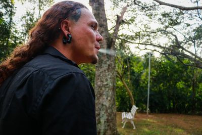 Man with long hair exhaling smoke against trees in forest