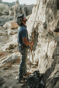 Hiker looking up while holding climbing rope by rock formation