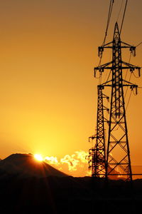 Low angle view of electricity pylon against sky during sunset