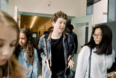 Male gesturing while talking to female friend in school corridor during lunch break