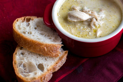 Fresh bread and a red crock of soup with rice and chicken pieces