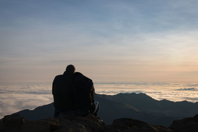 Rear view of man sitting on rock against sky