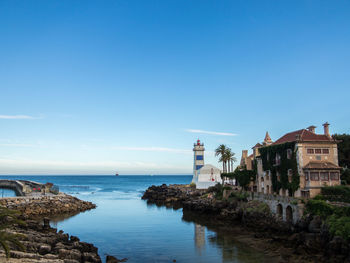 Buildings by sea against clear blue sky