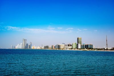 Sea by buildings against blue sky