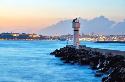 Lighthouse by sea against sky during sunset