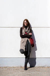 Full body smiling woman with arms crossed against white wall