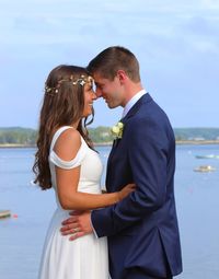 Young couple standing on sea shore against sky