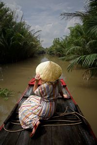 Rear view of woman wearing asian style conical hat while sitting on boat in lake