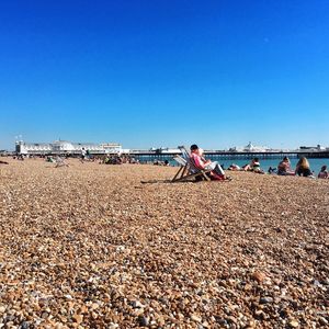 People on beach against clear blue sky