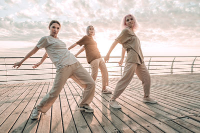 Full length of friends standing by railing against sea