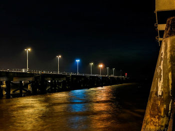 Illuminated bridge over river against sky at night