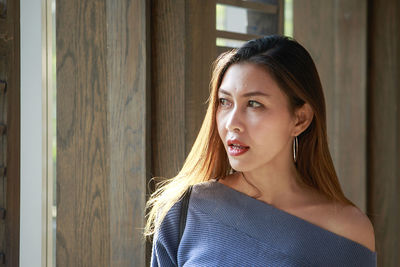 Thoughtful beautiful woman looking through window while standing at home