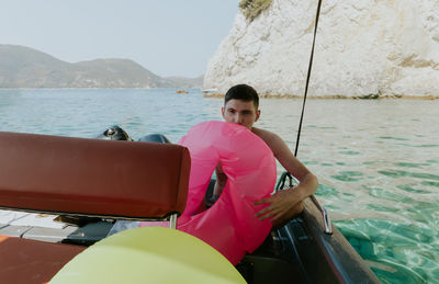 A young guy inflates a lifebuoy while sitting in a boat.