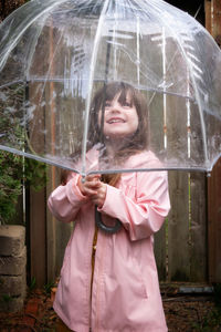 Smiling girl holding umbrella while standing outdoors during rain