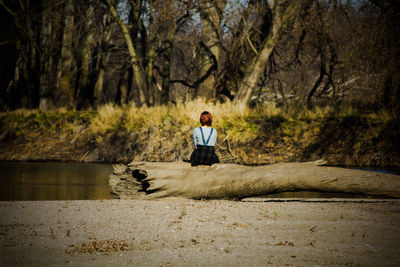 Woman sitting on log against trees