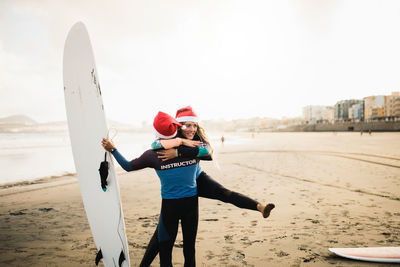 Woman embracing man holding surfboard at beach