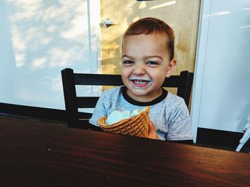 Portrait of smiling boy eating ice cream while sitting on table at home