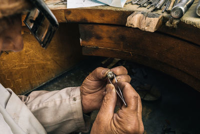 Side view of crop unrecognizable male goldsmith in glasses holding tweezers with diamond while creating jewelry accessory at workbench