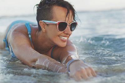 Close-up of smiling young woman lying at beach while wearing sunglasses